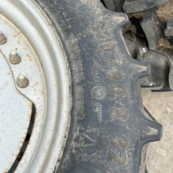 Close-up of a muddy tractor tire with a knobby tread beside a white, rusted wheel rim.