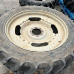Two large rugged tractor tires with metal rims stacked on a rough concrete surface, one rusty rim visible at the front