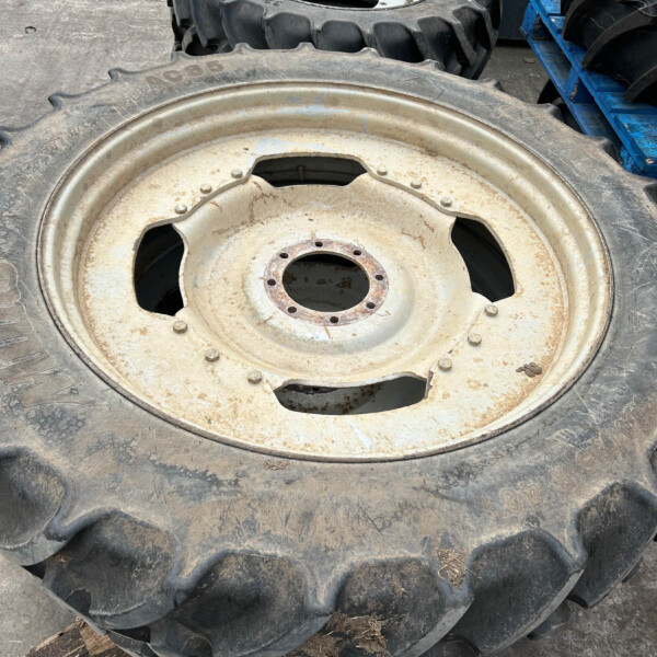 Two large rugged tractor tires with metal rims stacked on a rough concrete surface, one rusty rim visible at the front