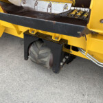 Close-up of yellow industrial machine parts with a rusted metal belt and guard on concrete ground.