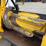 Close-up of a yellow industrial machine with rusted metal rollers and worn paint, outdoors on concrete surface.