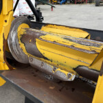 Close-up of yellow industrial machinery with rusted metal rollers and chipped paint, outdoors in a equipment yard