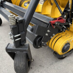 Close-up of a heavy yellow and black construction machine hitch with hydraulic pins and steel frame components.