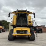 Front view of a large yellow earthmoving machine with oversized tracks, set in a yard under a cloudy sky.