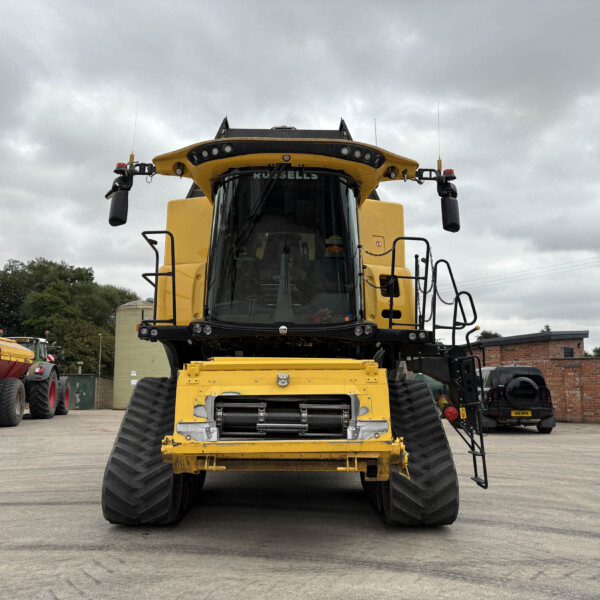Front view of a large yellow earthmoving machine with oversized tracks, set in a yard under a cloudy sky.