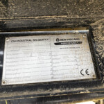 Close-up of a dusty equipment ID plate showing CNH Industrial Belgium and New Holland Agriculture logos and model data.