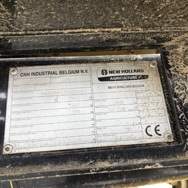 Close-up of a dusty equipment ID plate showing CNH Industrial Belgium and New Holland Agriculture logos and model data.
