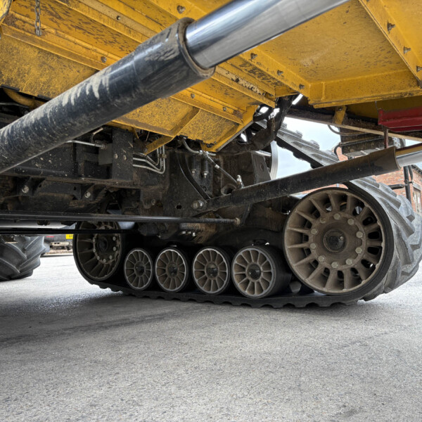 Underside of a yellow construction vehicle showing large metal tracks and hydraulic piping.