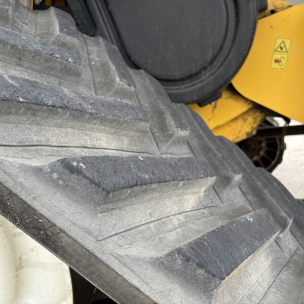 Close-up of large black rubber tracks with a yellow industrial machine frame and a small warning sticker in the background