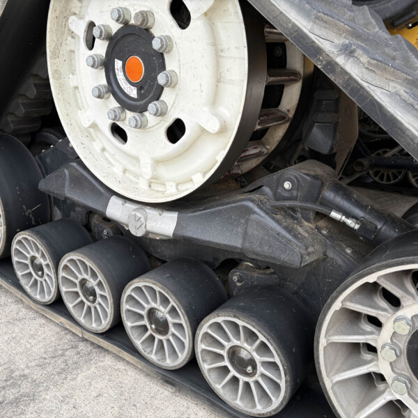 Close-up of a tracked construction machine's wheel and track system, showing bolts and a yellow body behind it.