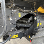 Section of heavy equipment chassis with wiring harnesses and yellow warning stickers.
