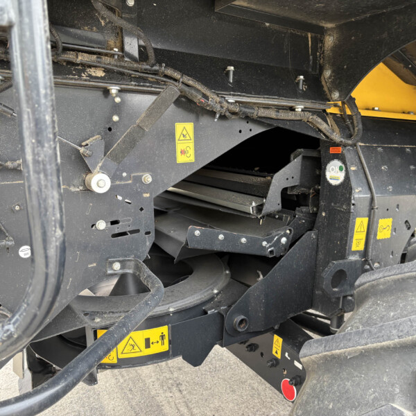 Section of heavy equipment chassis with wiring harnesses and yellow warning stickers.