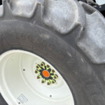 Close-up of a large tractor tire with a white rim, showing thick tread and colorful center bolts around an orange hub cap.