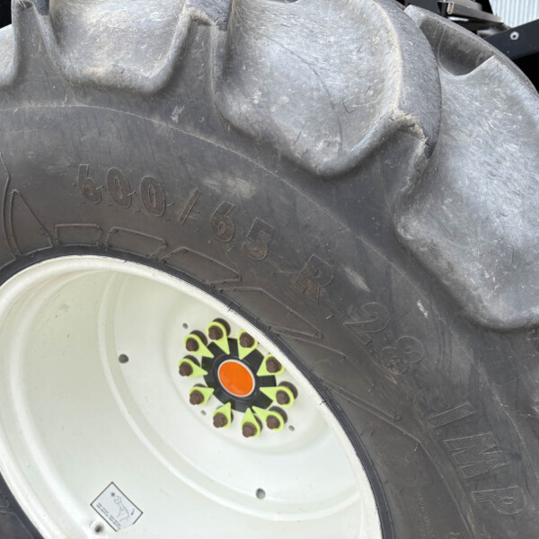 Close-up of a large tractor tire with a white rim, showing thick tread and colorful center bolts around an orange hub cap.