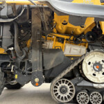Close-up of a yellow agricultural machine's underside showing belts, pulleys, and exposed components.