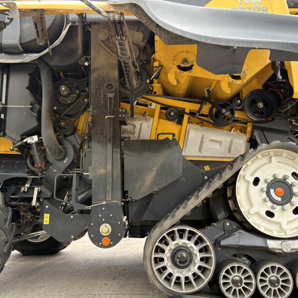Close-up of a yellow agricultural machine's underside showing belts, pulleys, and exposed components.