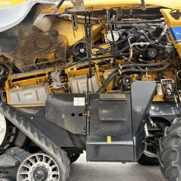 Close-up of the exposed belts, pulleys, and hydraulic lines inside a yellow agricultural combine harvester engine compartment.