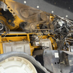 Close-up of yellow industrial machinery showing belts and pulleys with dusty, greasy components and a large tire in the foreground