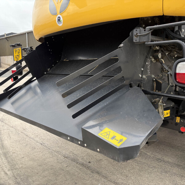 Rear view of a large yellow industrial machine showing a wide black intake/chute and multiple angled bars, with red tail lights on the right side and a license plate area visible.