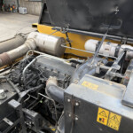 Close-up of an industrial machine engine bay with hoses, metal tanks, and a yellow frame and warning labels in view.