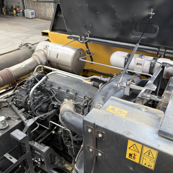 Close-up of an industrial machine engine bay with hoses, metal tanks, and a yellow frame and warning labels in view.