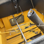 Interior view of a yellow industrial machine with black side panels, metal supports, and a large gray duct/tube running through the frame