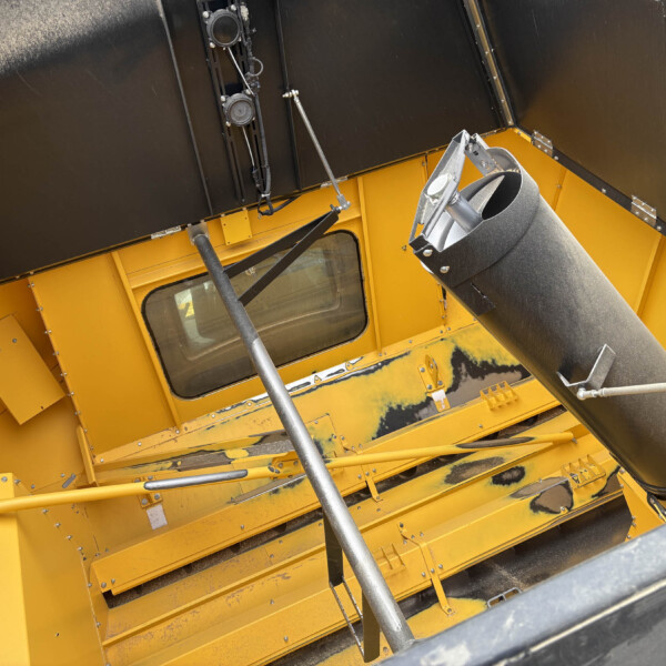 Interior view of a yellow industrial machine with black side panels, metal supports, and a large gray duct/tube running through the frame