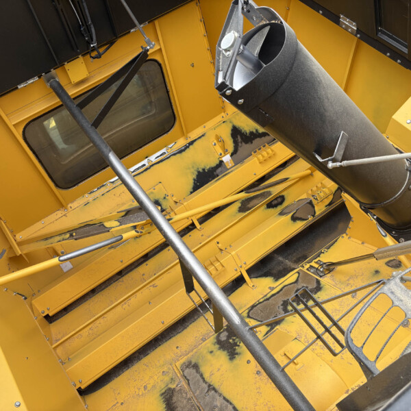 Interior view of yellow industrial equipment showing a large black duct/chute and supporting metal rods.