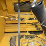 Close-up view of yellow industrial machinery interior, with metal panels, bolts, and a large black duct running along the right side.
