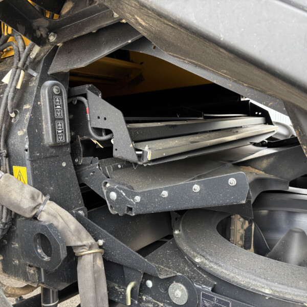 Close-up of a heavy machinery interior showing wiring harnesses, hydraulic hoses, and metal framing around a control panel with up/down arrows.