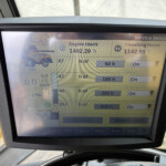 Close-up of a digital control display on a machine showing Engine Hours 1402.29 h and Threshing Hours 1142.99 h with other hours and setup indicators nearby.
