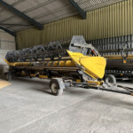 Yellow combine harvester header on a trailer inside a metal-clad warehouse, ready for storage or transport.