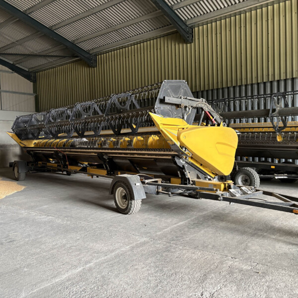 Yellow combine harvester header on a trailer inside a metal-clad warehouse, ready for storage or transport.