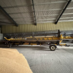 Industrial warehouse interior with corrugated metal walls and a yellow farming implement on a trailer inside.