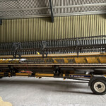 New Holland farm equipment header attached to a trailer, stored inside a metal-sided warehouse.