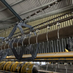Industrial textile machine with overhead rollers and multiple circular hooks along metal rods in a factory setting
