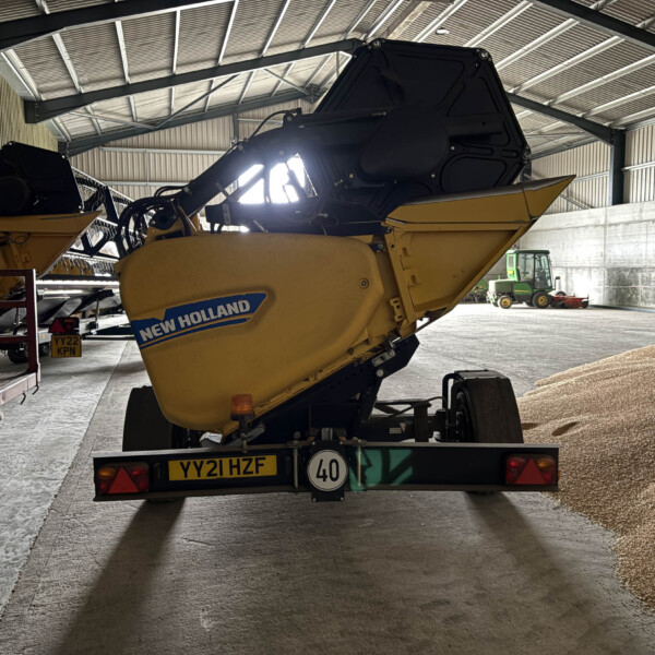 Rear view of a yellow New Holland combine harvester inside a large shed, with a green tractor in the background.