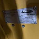 Metal identification plate on a yellow surface showing New Holland Agriculture branding and CNH Industrial Belgium, with country and model details visible.