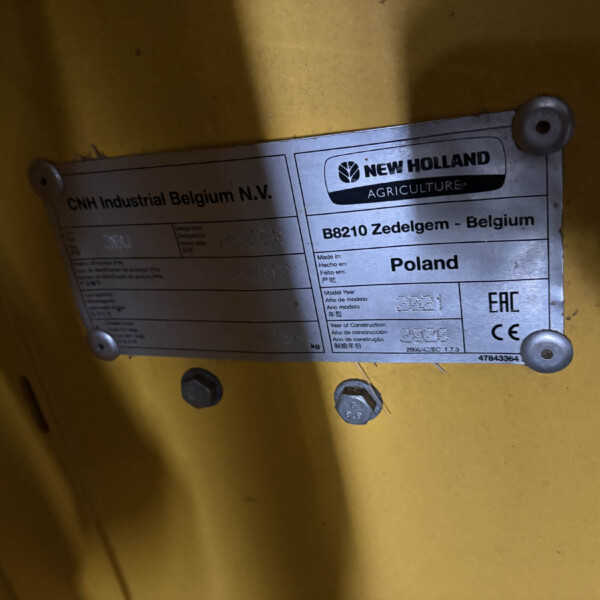 Metal identification plate on a yellow surface showing New Holland Agriculture branding and CNH Industrial Belgium, with country and model details visible.