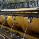 Close-up of a New Holland agricultural implement with curved metal tines and springs on a yellow frame.