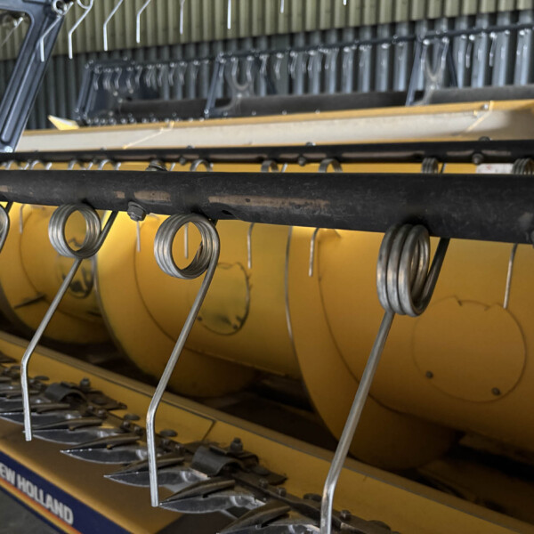 Close-up of a New Holland agricultural implement with curved metal tines and springs on a yellow frame.