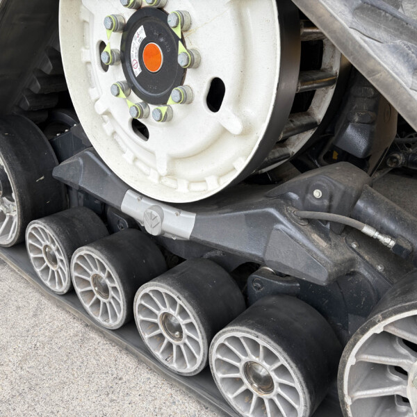 Close-up of a construction machine's rubber track and wheel assembly, showing a white wheel hub with orange center and bolts.