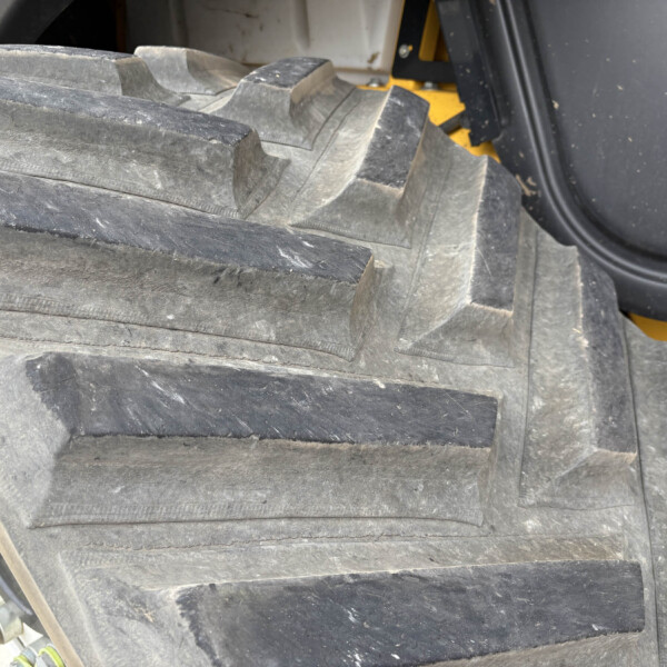 Close-up of a heavy equipment rubber track with large tread blocks; yellow machine frame visible in the background.