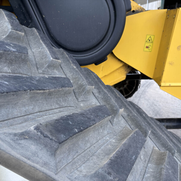 Close-up of a large black treaded tire with a yellow industrial machine body in the background.