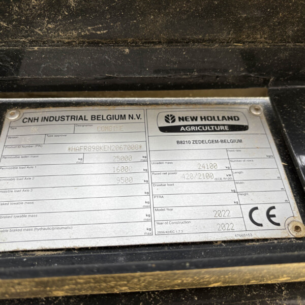 Close-up of a dusty metal data plate on a black surface; CNH Industrial Belgium N.V. and New Holland Agriculture branding visible.