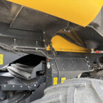 Close-up of black metal framework with yellow safety panels on heavy machinery, showing bolts and cables in a dusty environment.