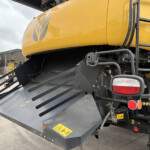 Close-up of a large yellow construction machine with black metal steps, ladder rungs, and rear lights; visible warning stickers and machinery components.