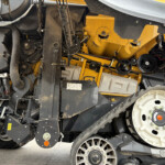 Close-up view of exposed machinery inside a yellow agricultural harvester, showing belts, pulleys, and metal framework.