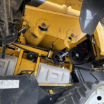 Close-up of yellow heavy machinery interior showing belts, pulleys, and exposed components with warning labels present in the area.