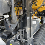 Close-up of a yellow and black industrial machine showing belts, hoses, metal frames and dusty components inside the chassis.
